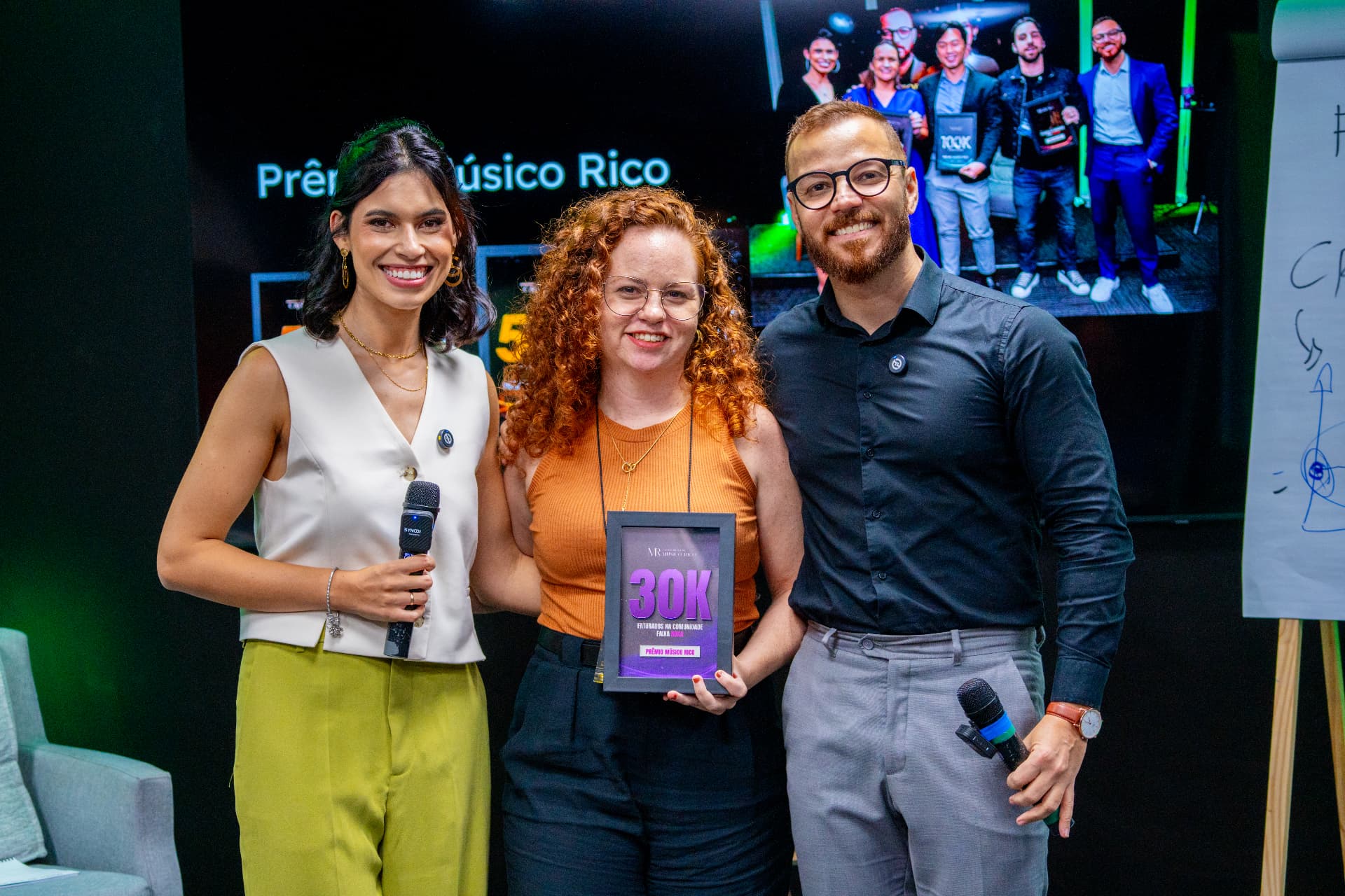 Participante recebendo placa de reconhecimento ao lado dos organizadores